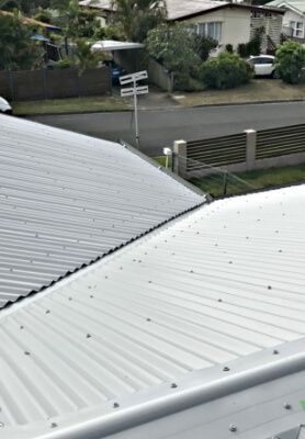 View from a rooftop over white corrugated roofs to a quiet residential street and houses beyond