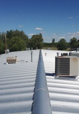 Rooftop with white metal panels, HVAC units, and a blue sky over trees in the distance