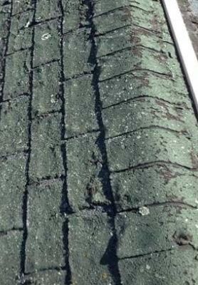Green textured roof shingles with a cracked seam running vertically down the center