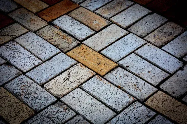 Diagonal brick pavement in gray, tan, and reddish tones with a dark vignette effect