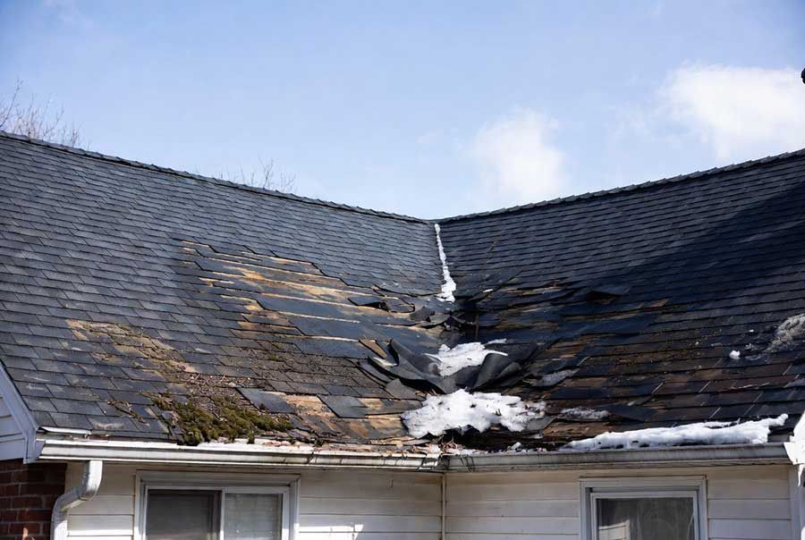 Damaged roof with charred shingles and a hole near the ridge above a house