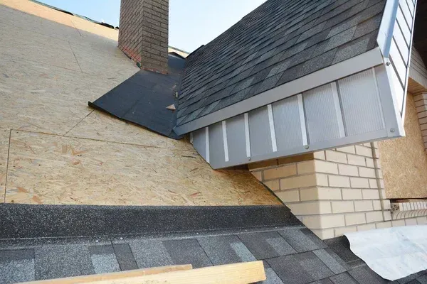 Damaged roof area with shingles, exposed underlayment, and brick chimney in a close-up exterior view