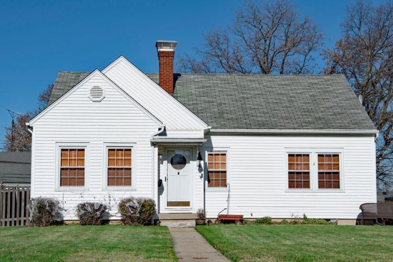 White house with gray roof, brick chimney, and front walkway under a clear blue sky