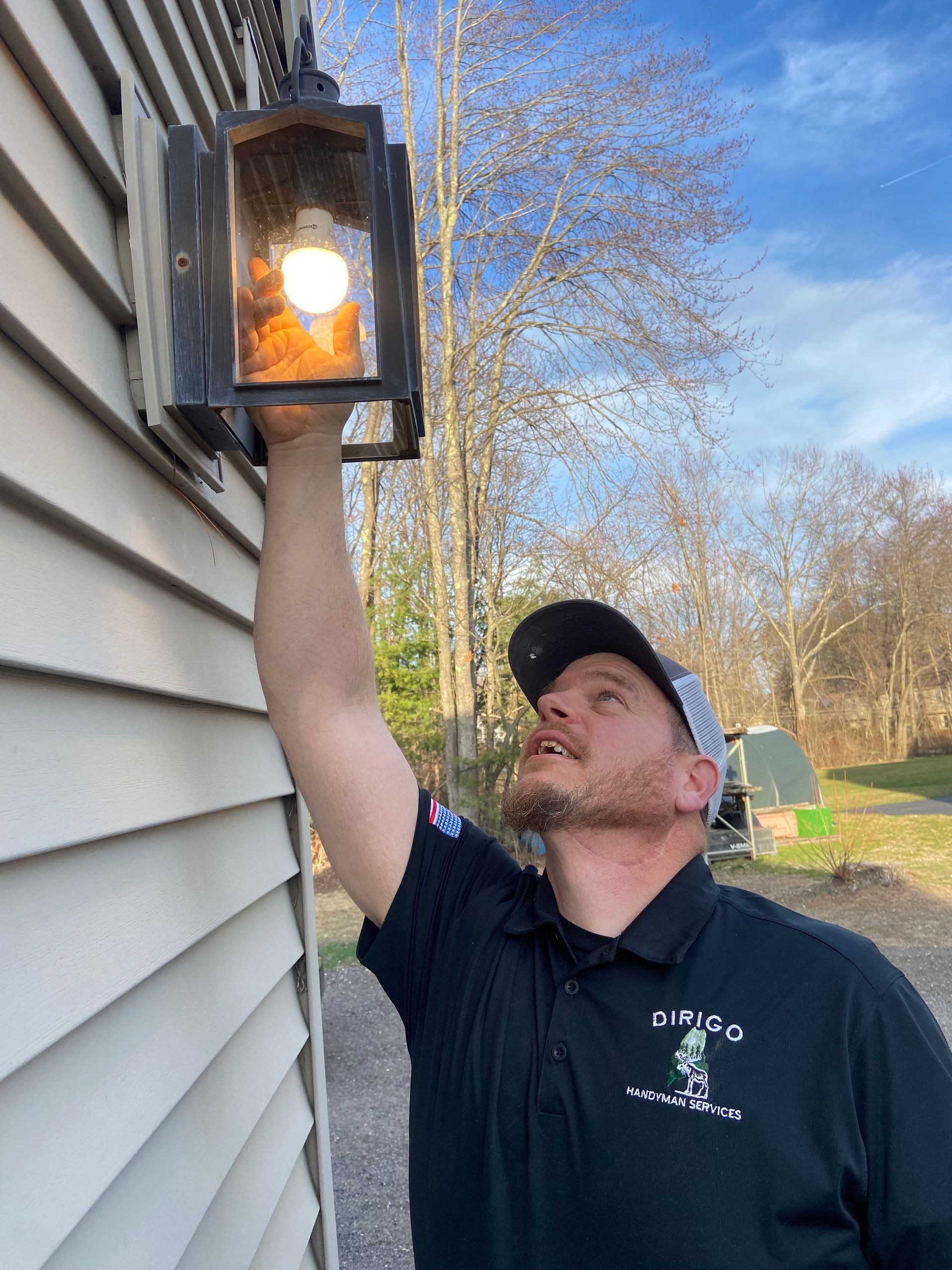 A man is fixing a light on the side of a house.
