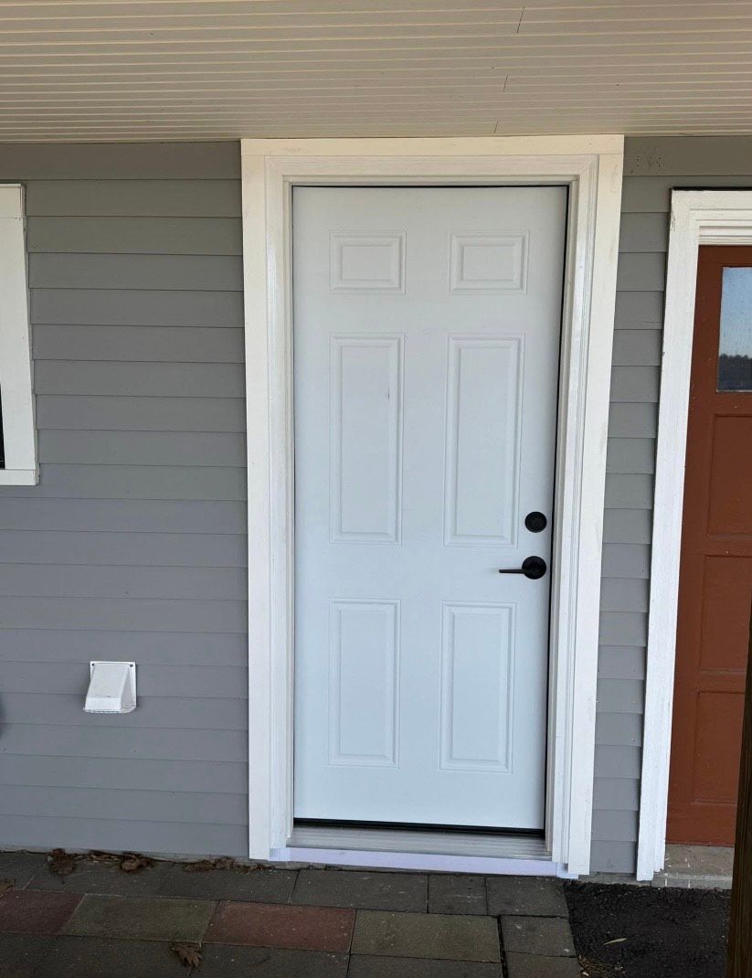 A white door is sitting on the side of a house next to a red garage door.