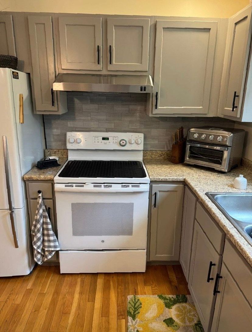 A kitchen with a stove , refrigerator , sink and toaster oven.