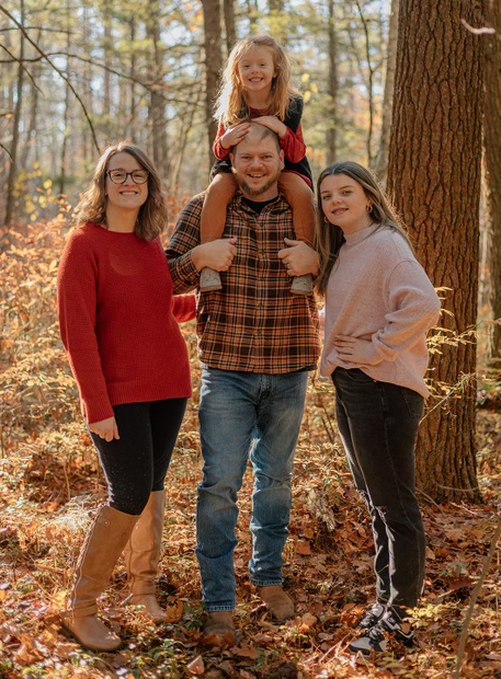 A family is posing for a picture in the woods.