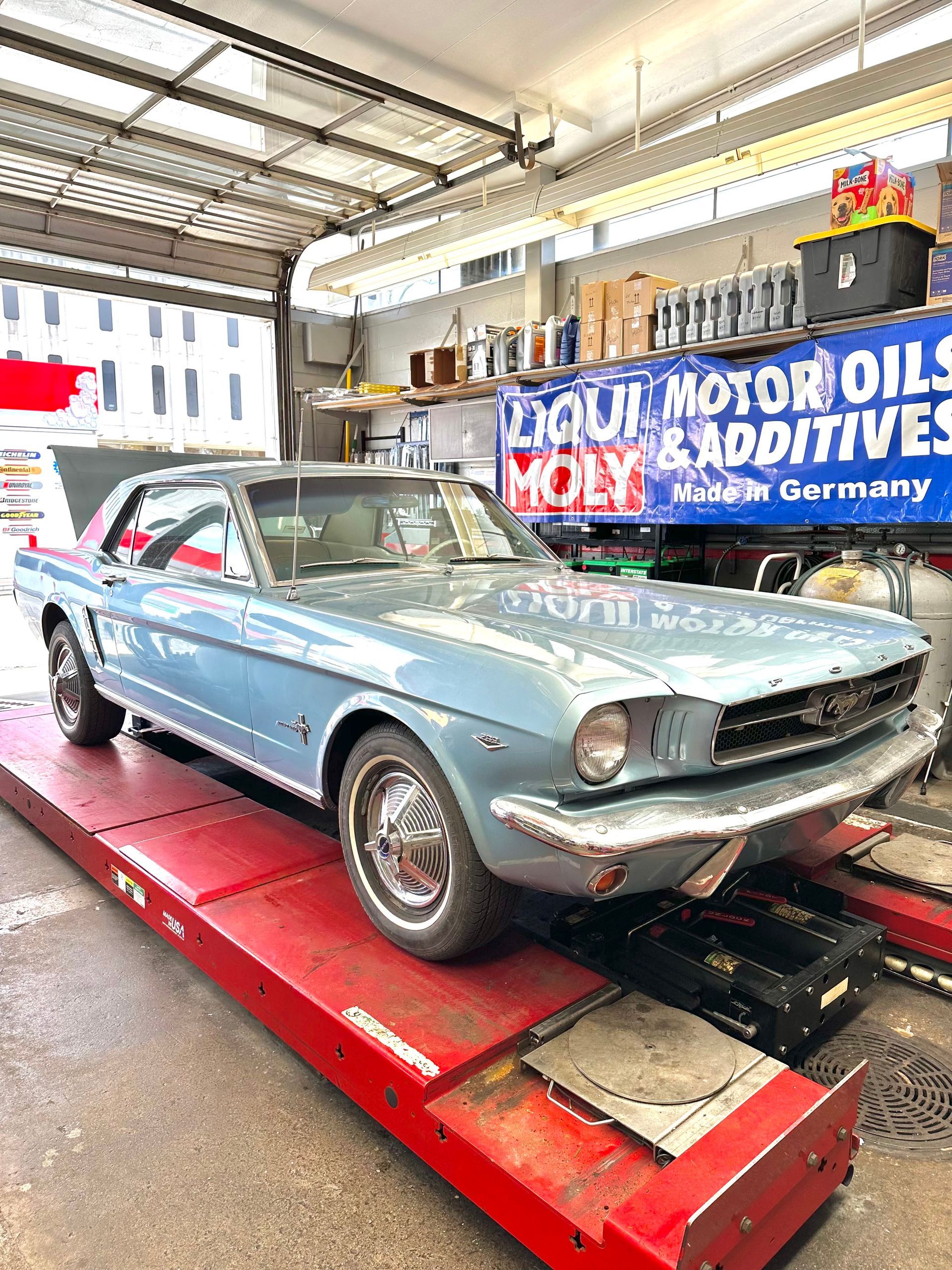 Classic blue Ford Mustang on a red lift inside a garage, with shelves of oil in the background | Reeder's Auto & Tire Blog