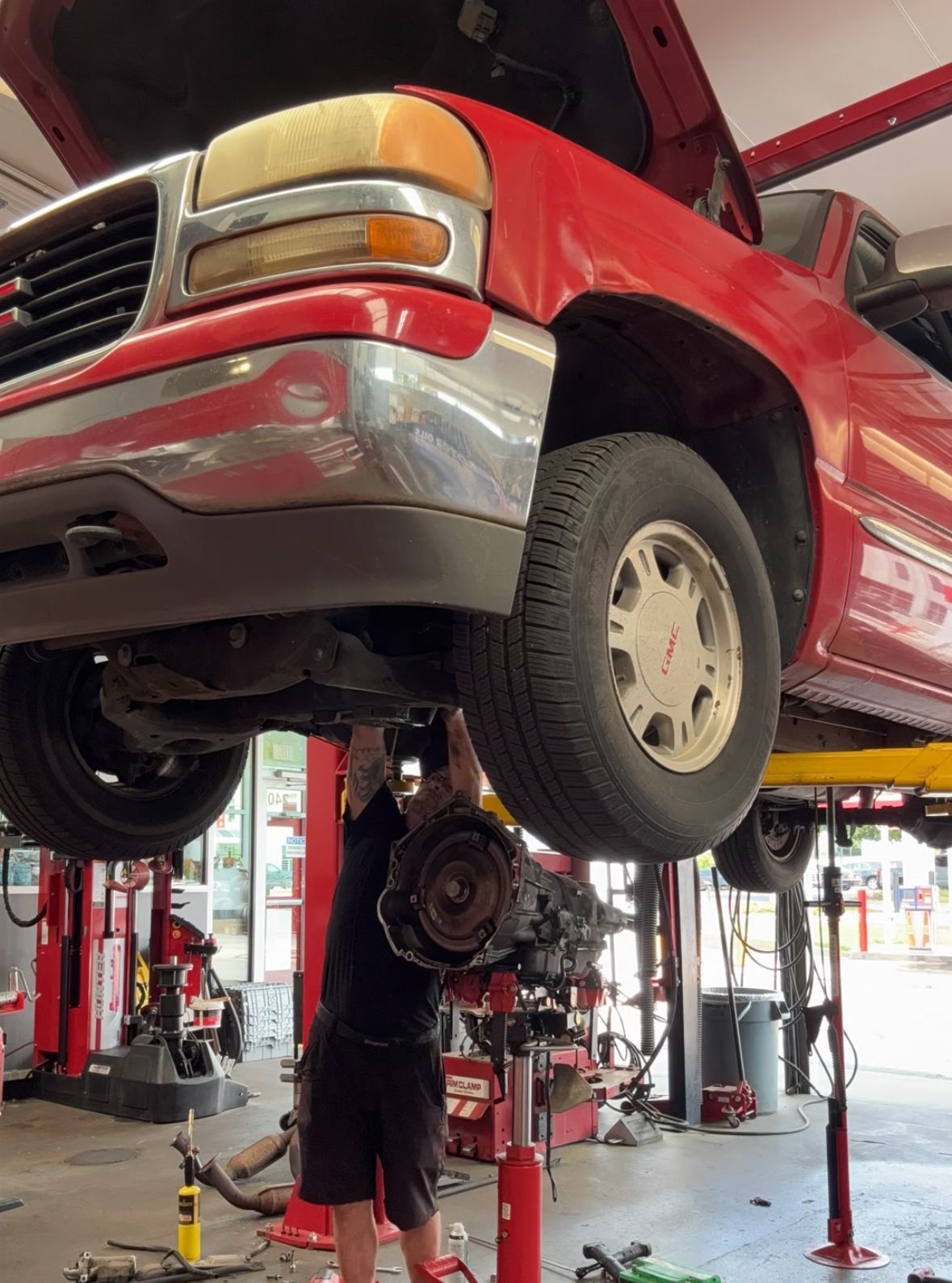 Mechanic working on a red GMC truck raised on a lift in a garage | Reeder's Auto & Tire Blog
