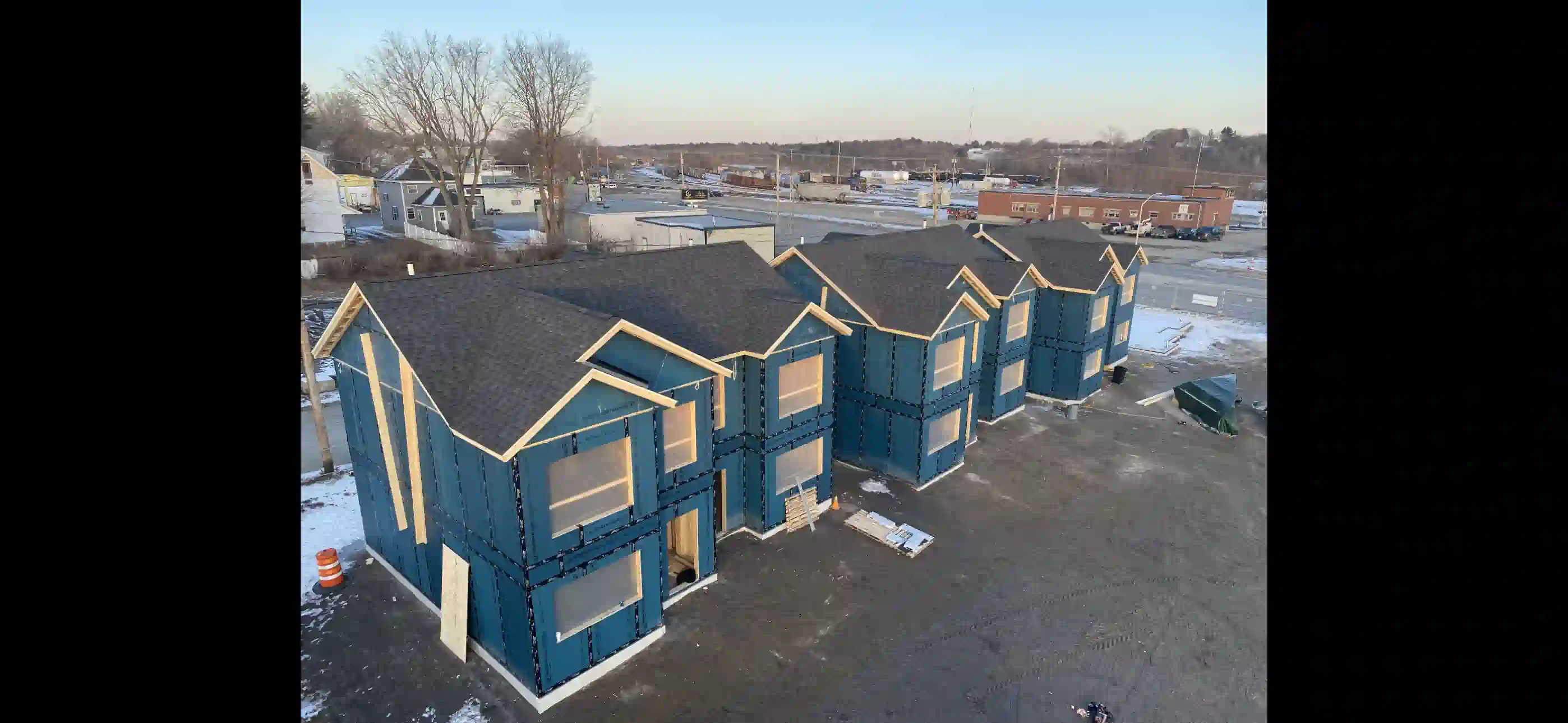 Wooden deck attached to a house with stairs, black railing, and support posts over a gravel area.