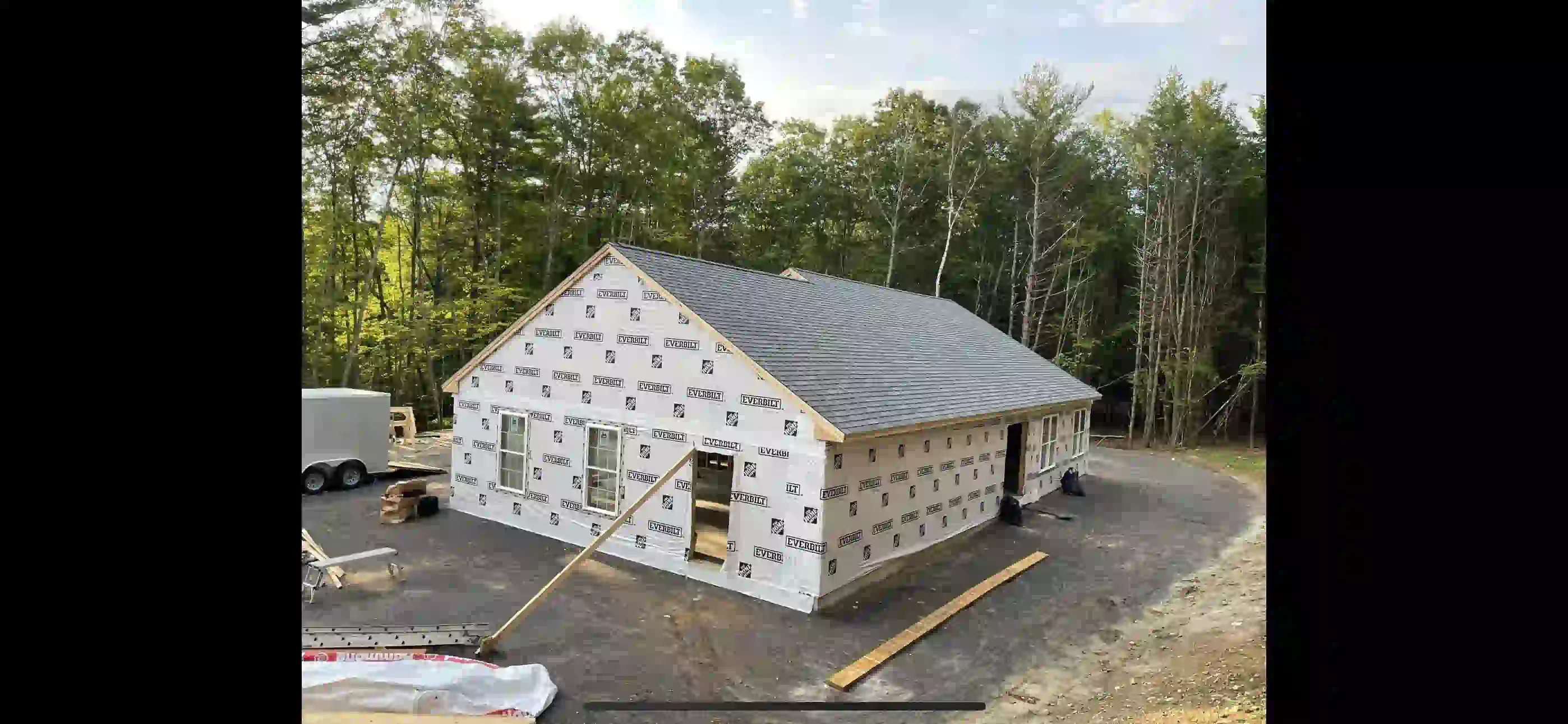 Wooden deck attached to a house with stairs, black railing, and support posts over a gravel area.