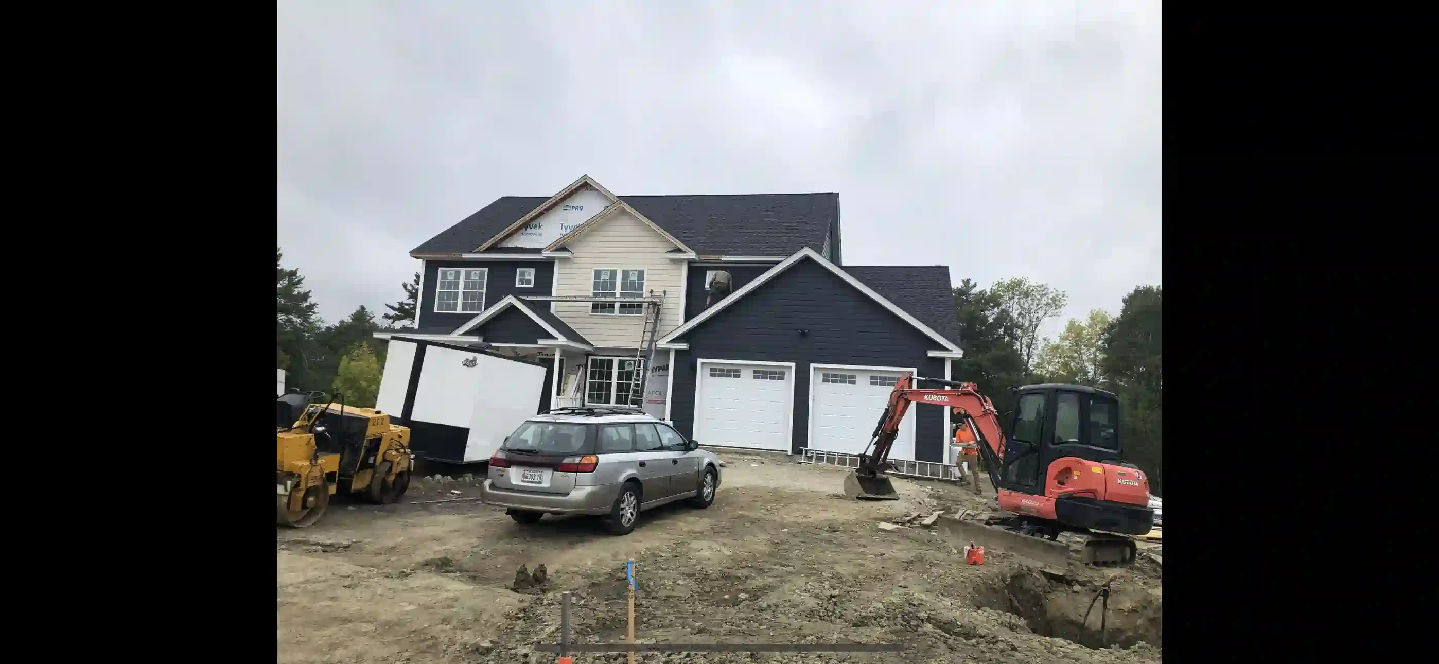 Wooden deck attached to a house with stairs, black railing, and support posts over a gravel area.