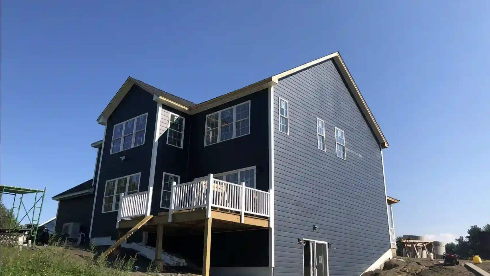 Wooden deck attached to a house with stairs. Black railings, tan siding, and a gravel base.