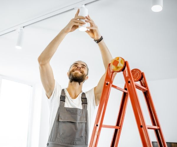 A man is standing on a ladder holding a light bulb.