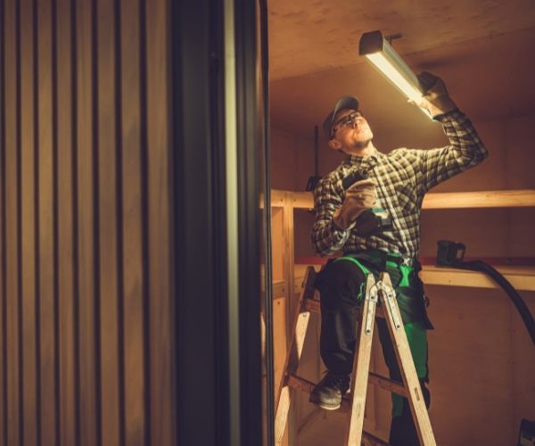 A man is sitting on a ladder working on a light fixture
