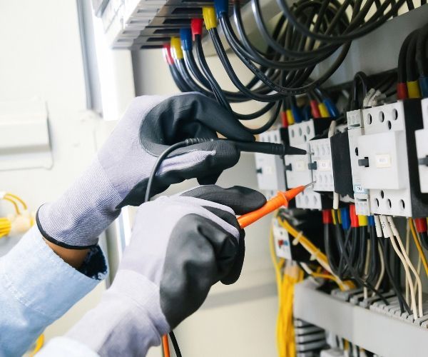 An electrician is working on an electrical box with a multimeter.