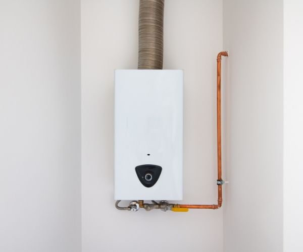 A white water heater is connected to a copper pipe on the wall.