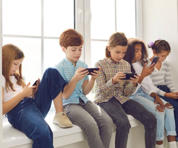 A group of children are sitting on a window sill looking at their phones.