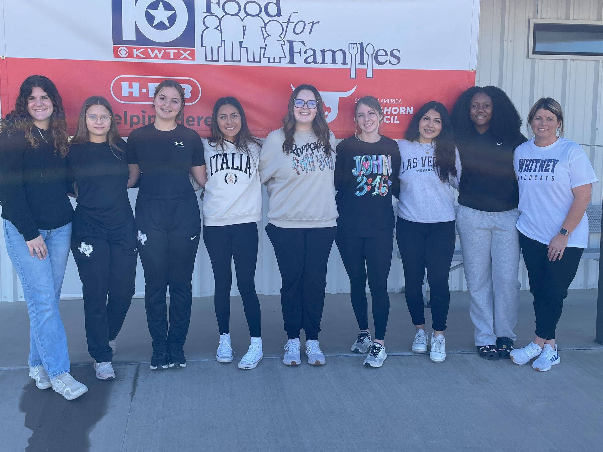 A group of women are posing for a picture in front of a sign that says food for families.