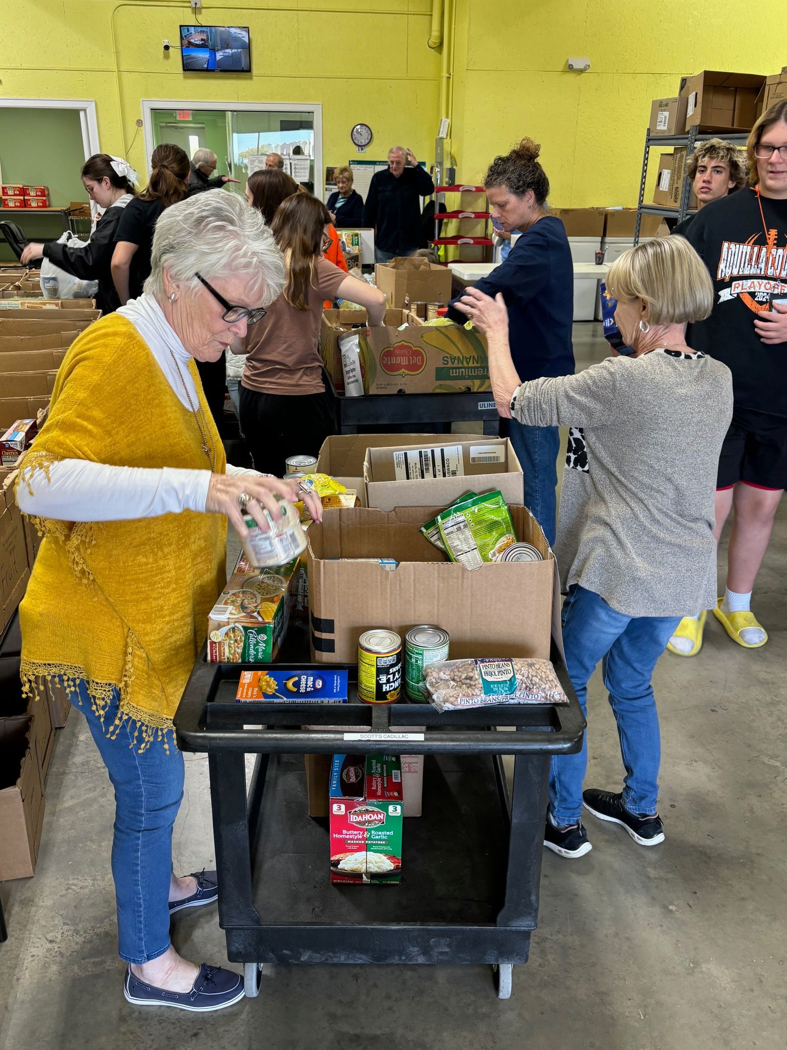Three women are standing around a table filled with boxes of food.