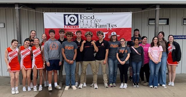 A group of people are standing in front of a sign that says food for families.