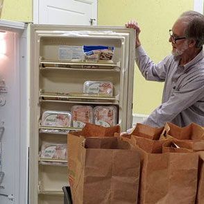 A man is standing in front of a refrigerator filled with bags of food.