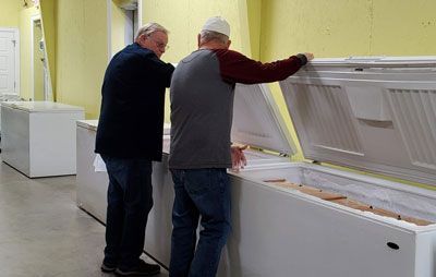 Two men are looking into a freezer in a store.