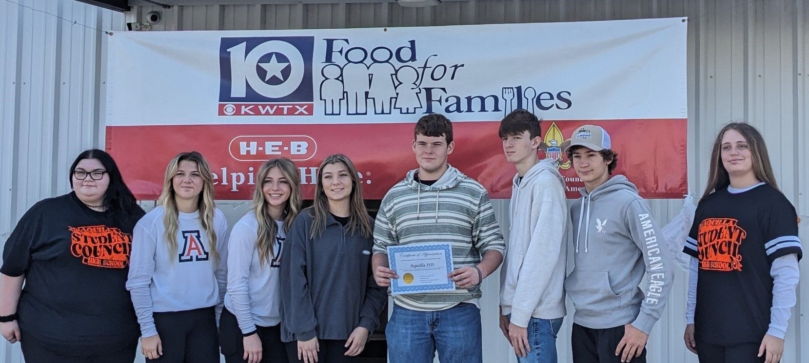 A group of people are standing in front of a sign that says food for families.