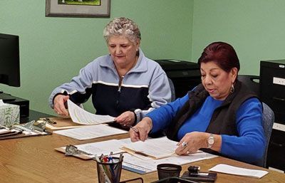 Two women are sitting at a desk looking at papers.