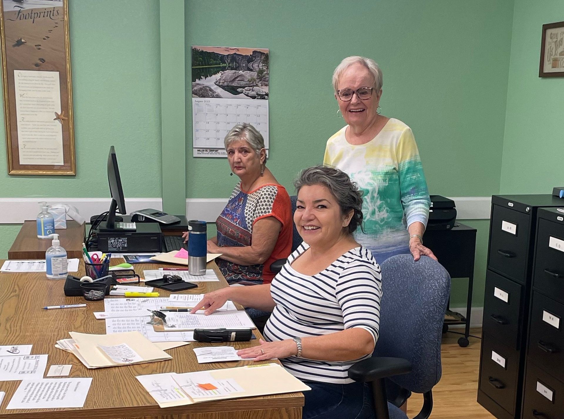 Three women are sitting at a desk in an office.