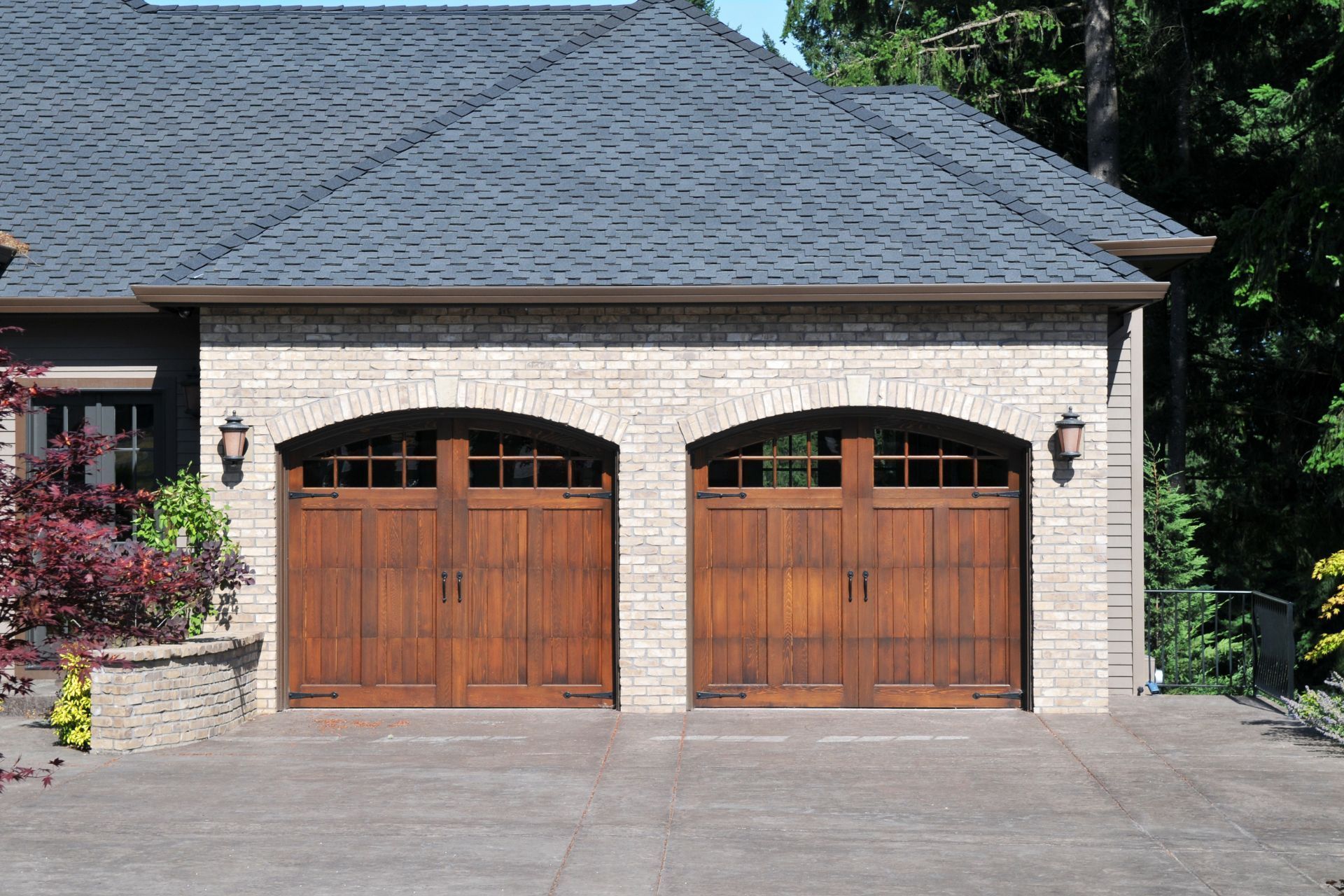 Two arched wooden garage doors with glass-paneled tops set in a light stone facade of a house.
