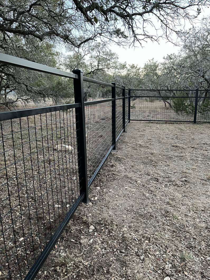 A black fence with a gate in the middle of a field.