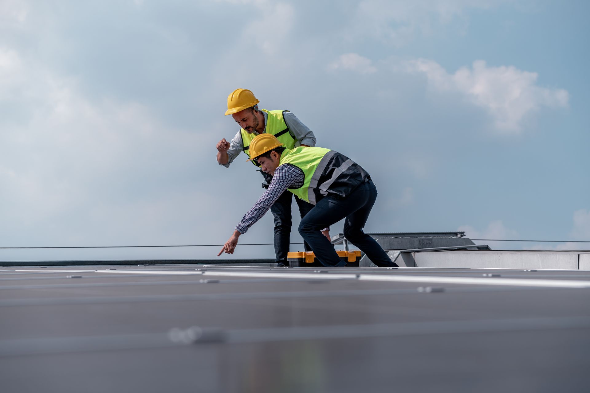Roofer in orange hard hat, hammers metal flashing on a white commercial roof.