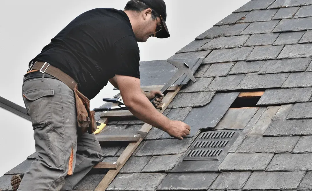 Roofer in safety gear, kneeling on a rooftop, hammering shingles.