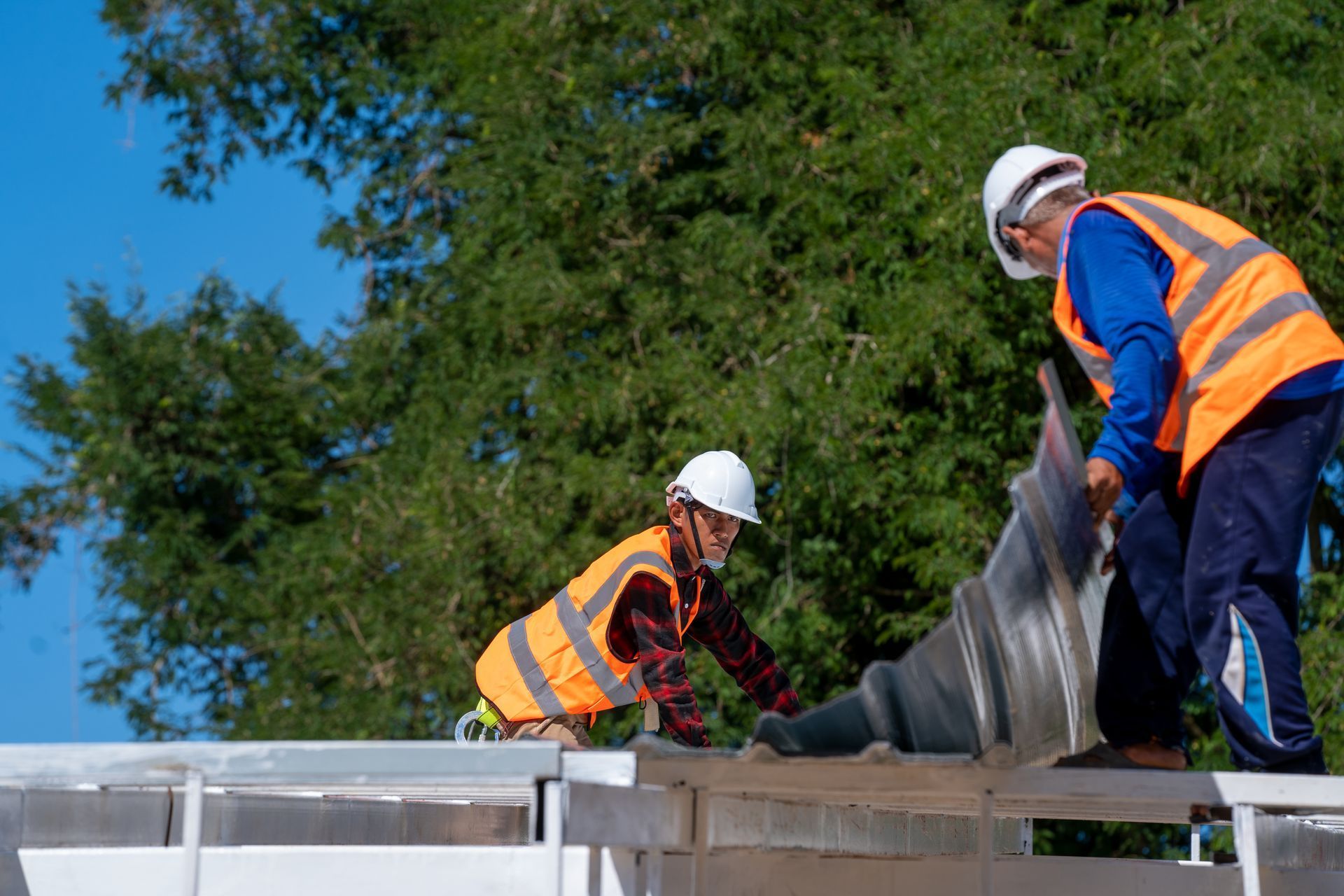 Construction worker with tablet smiles, flanked by colleagues on a rooftop, studying blueprints.
