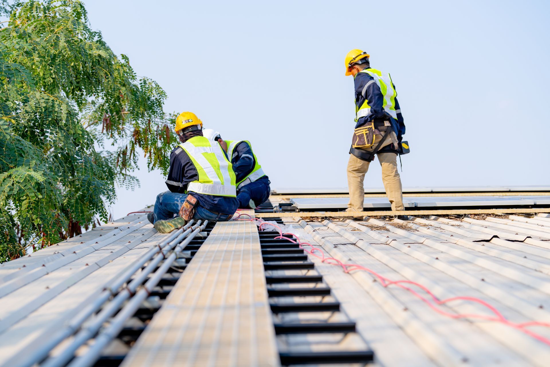Two construction workers on a rooftop, studying blueprints under a blue sky. One points, the other holds the paper.