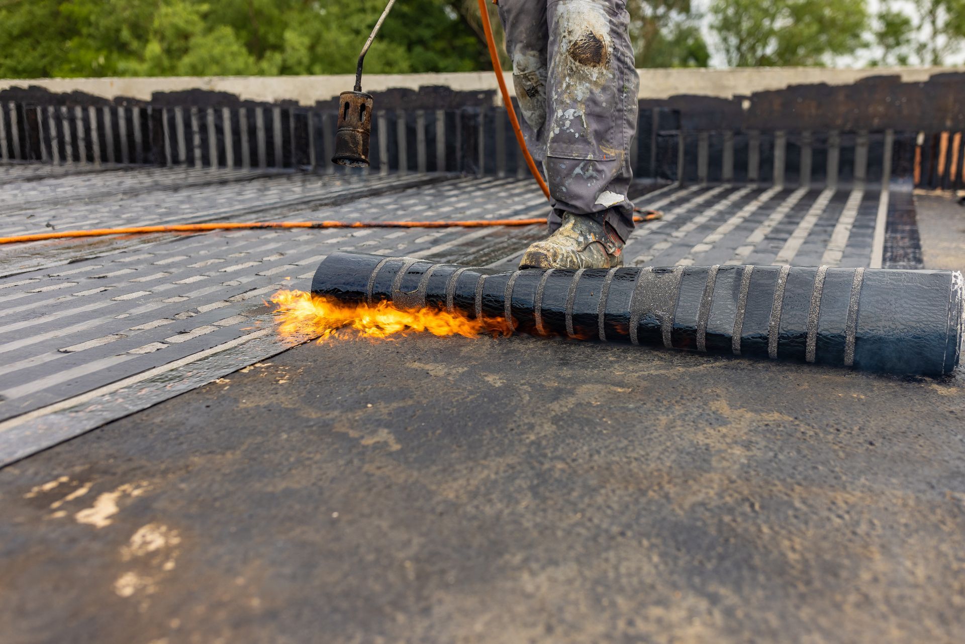 Roofer using a torch to install roofing material on a flat roof.