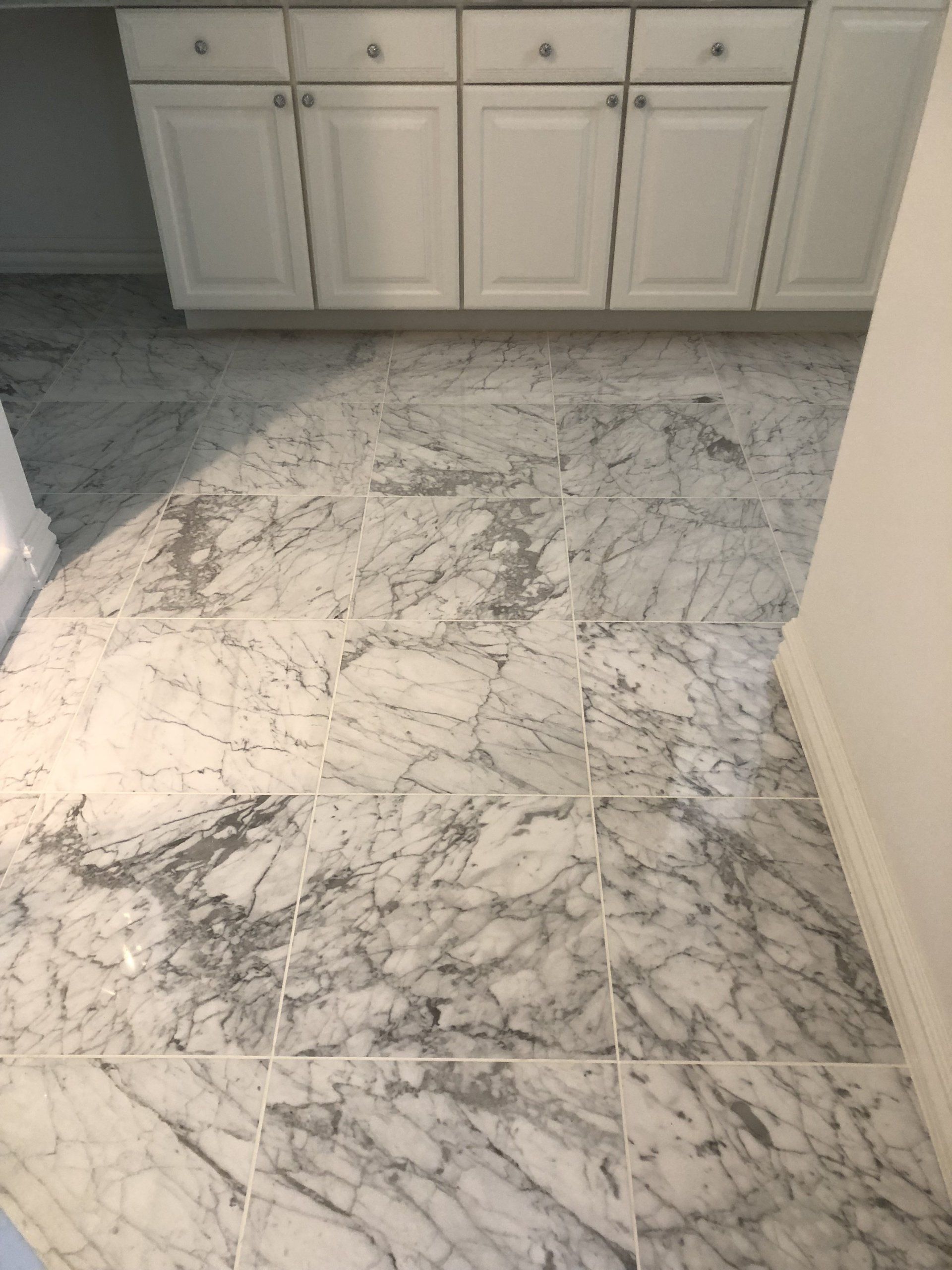A kitchen with a marble floor and white cabinets.