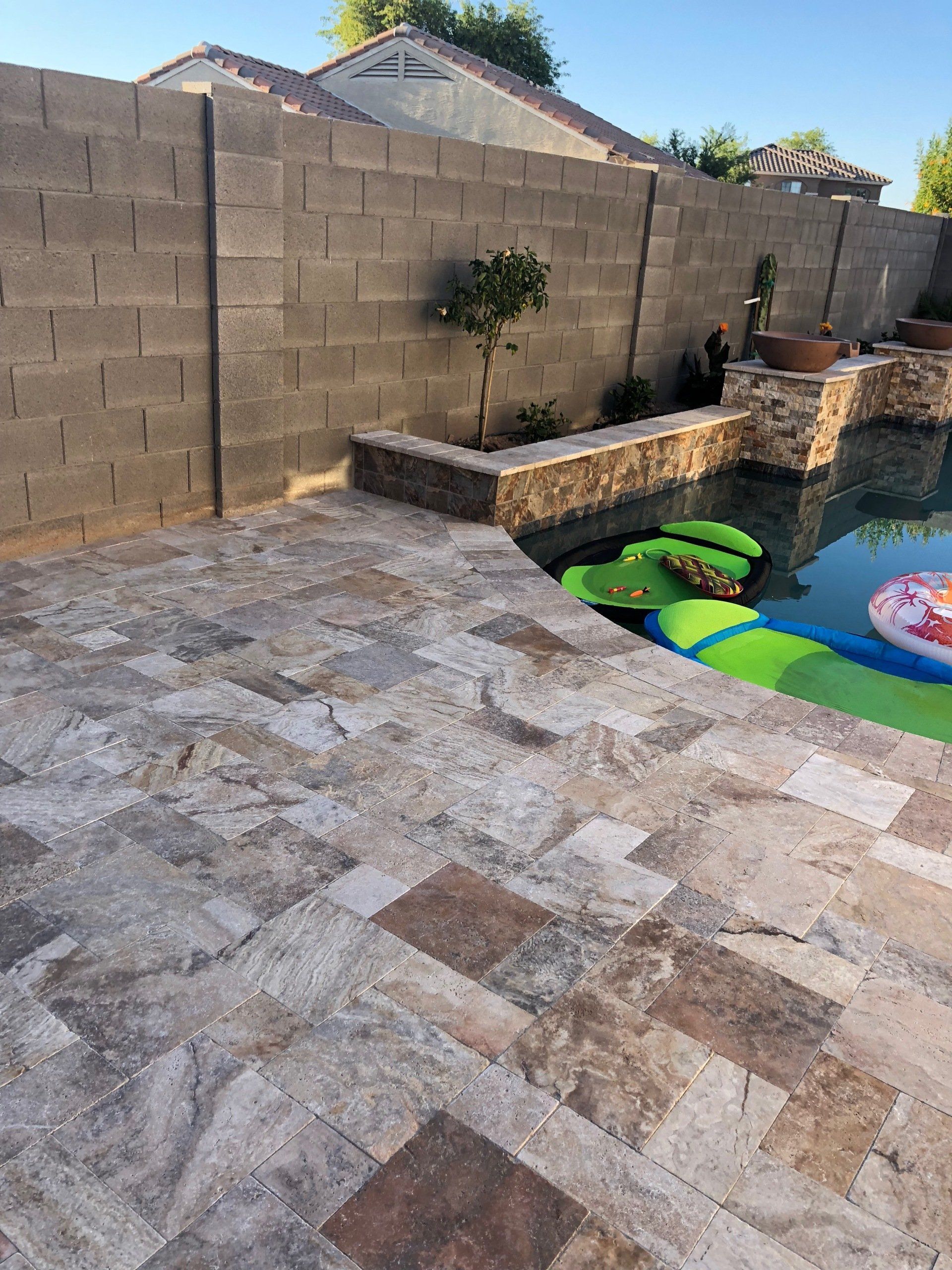 A brick wall surrounds a swimming pool with a patio in front of it.