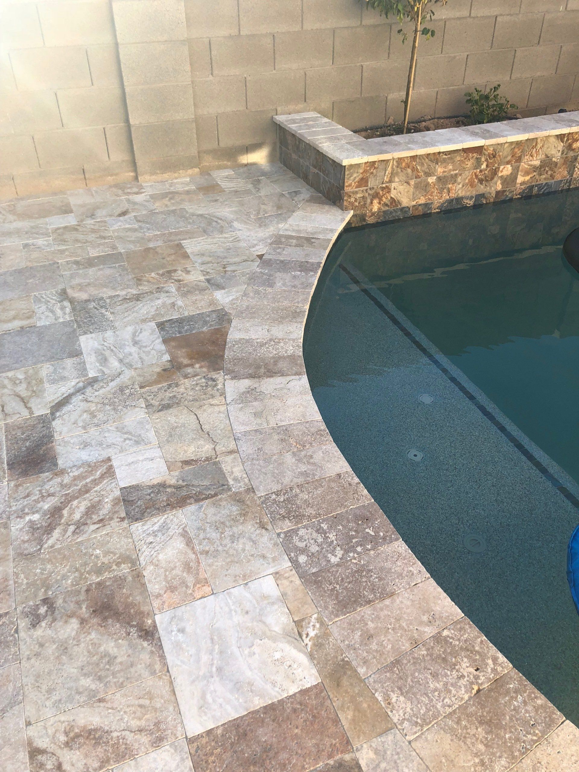 A swimming pool with a tiled patio next to it.