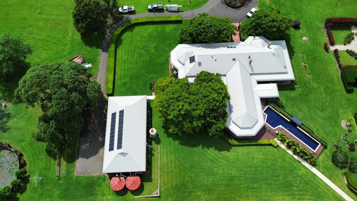 An Aerial View of a House With a Blue Roof in the Middle of a Lush Green Field — Tim Leach Metal Roofing in Wauchope, NSW