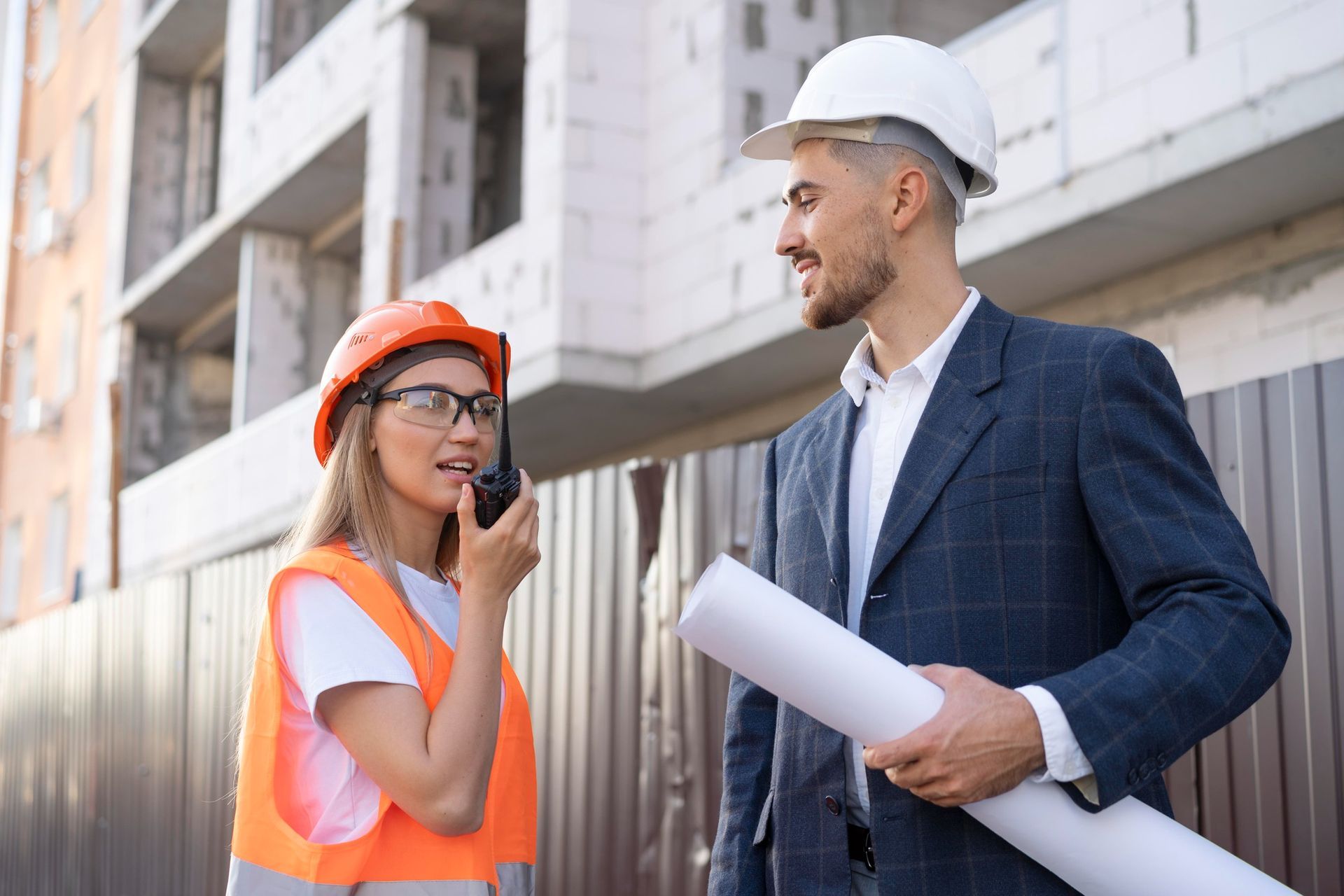 A man and a woman are talking on a walkie talkie on a construction site.