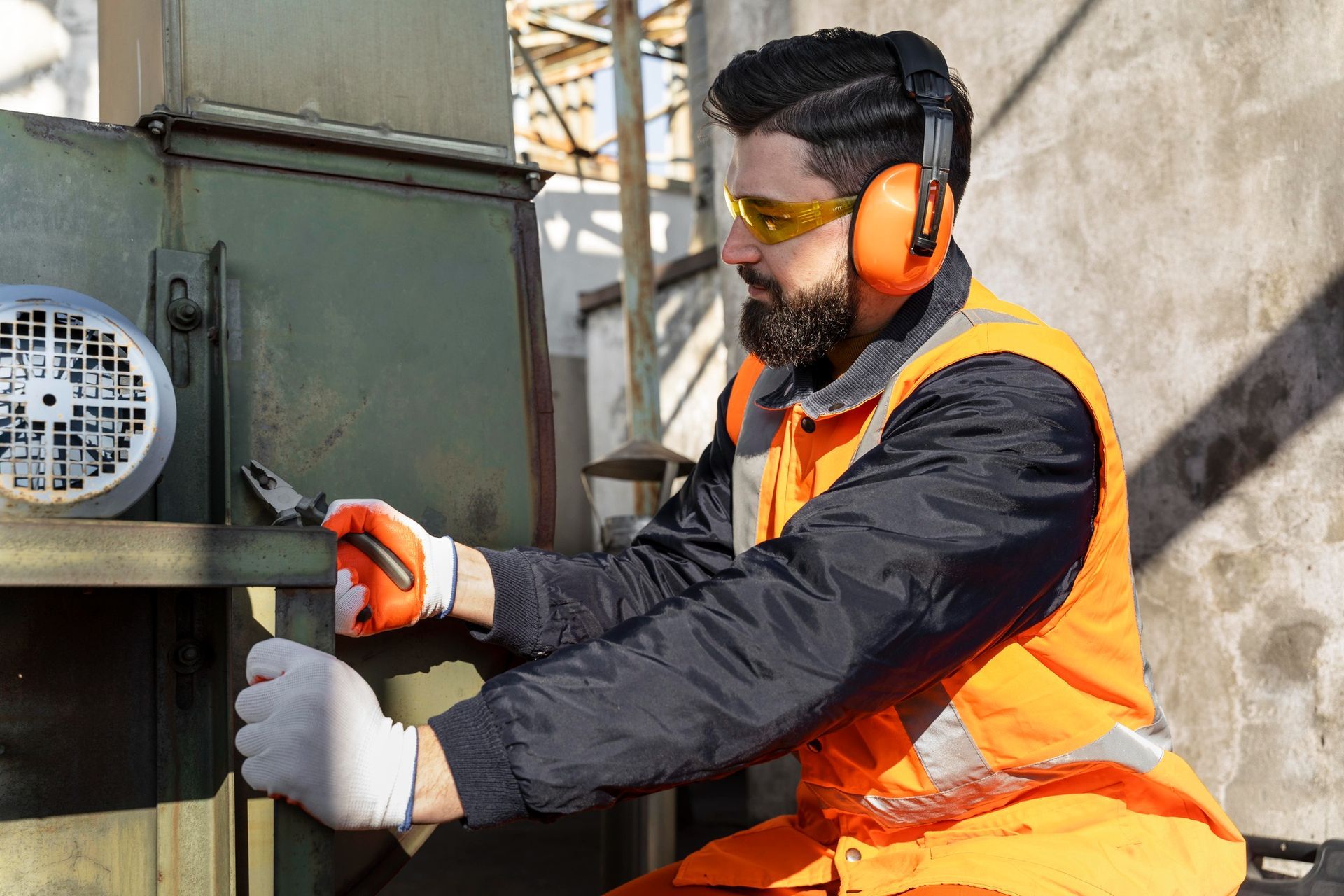 A man wearing ear muffs and safety glasses is working on a machine.