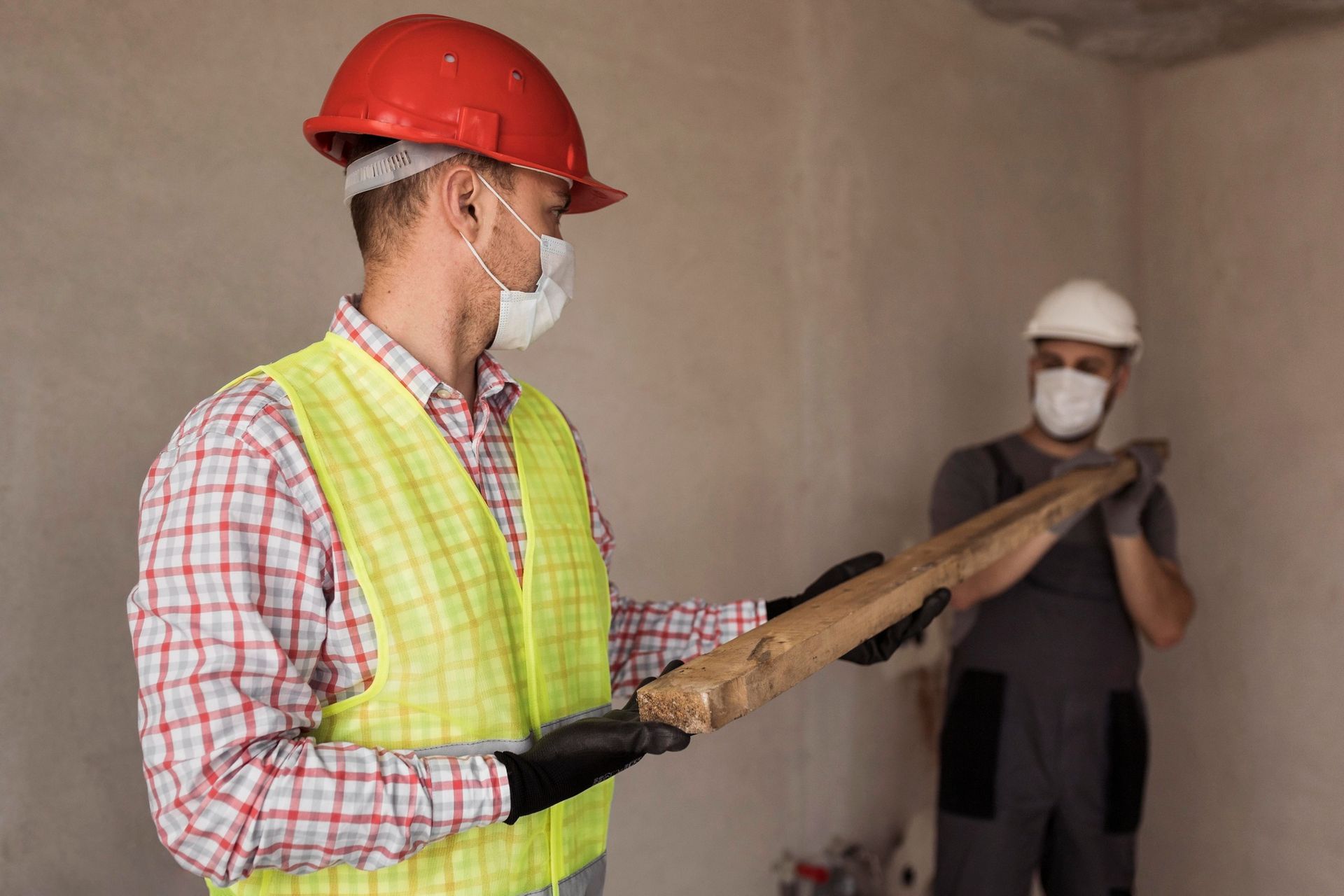 A man wearing a hard hat and a mask is holding a piece of wood.