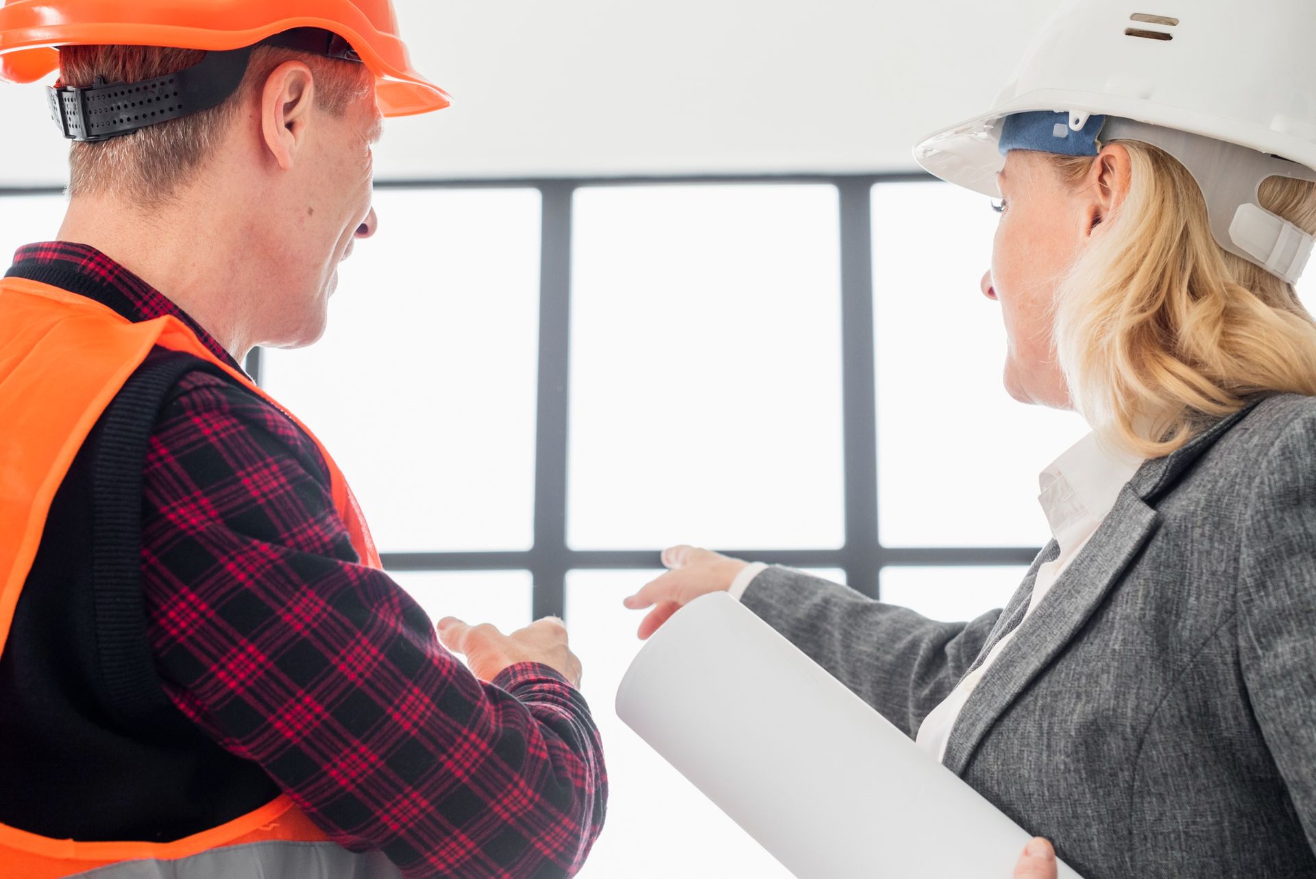 A man and a woman are shaking hands while looking at a blueprint.