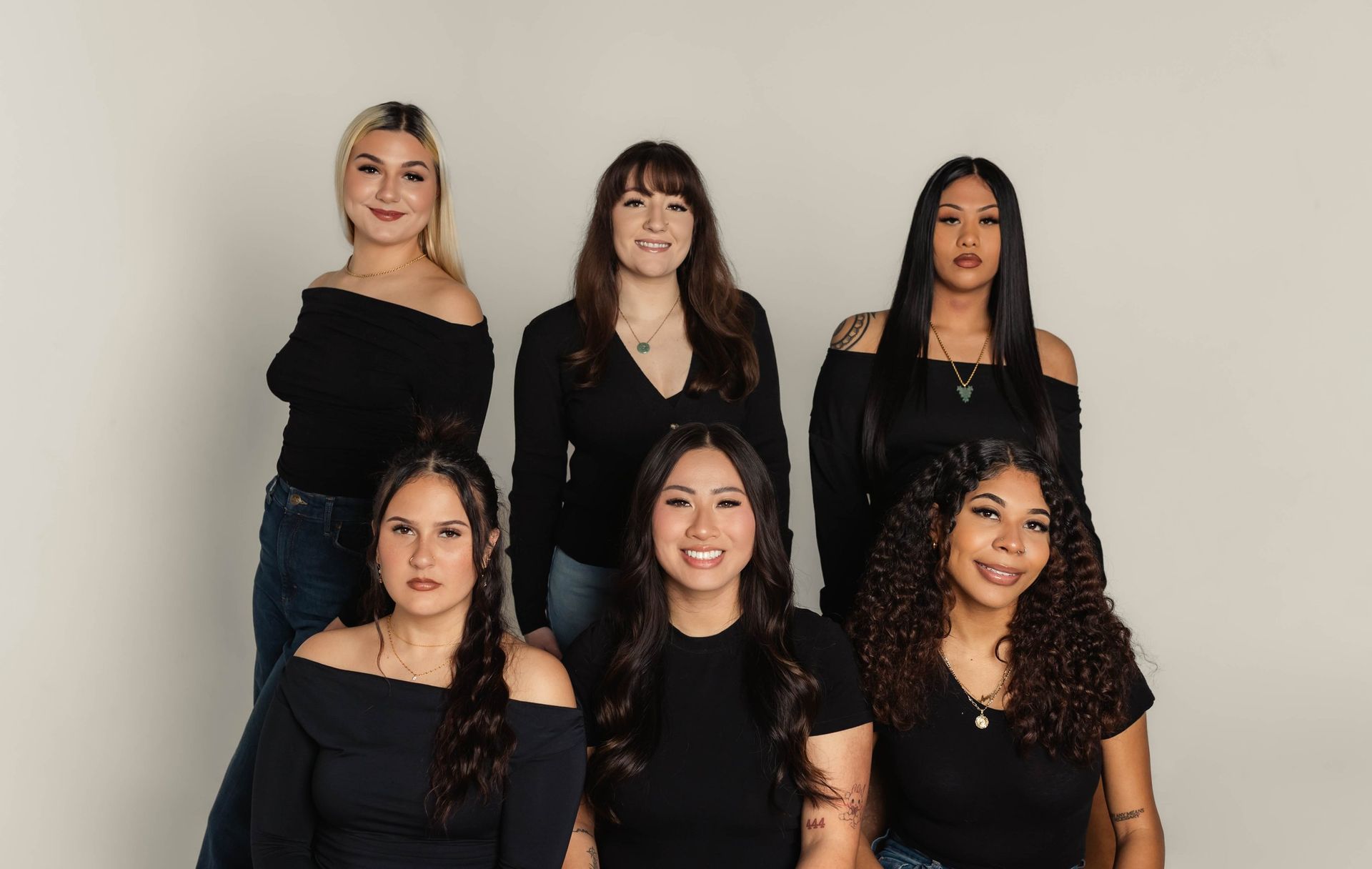 Six people in black tops and jeans pose in front of a white background.