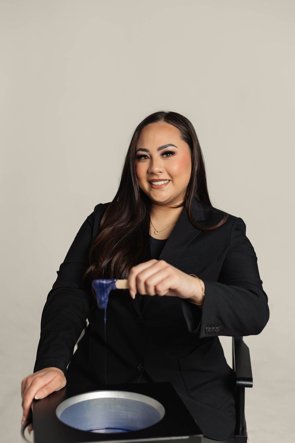 Woman in black suit holding wax applicator over wax warmer.