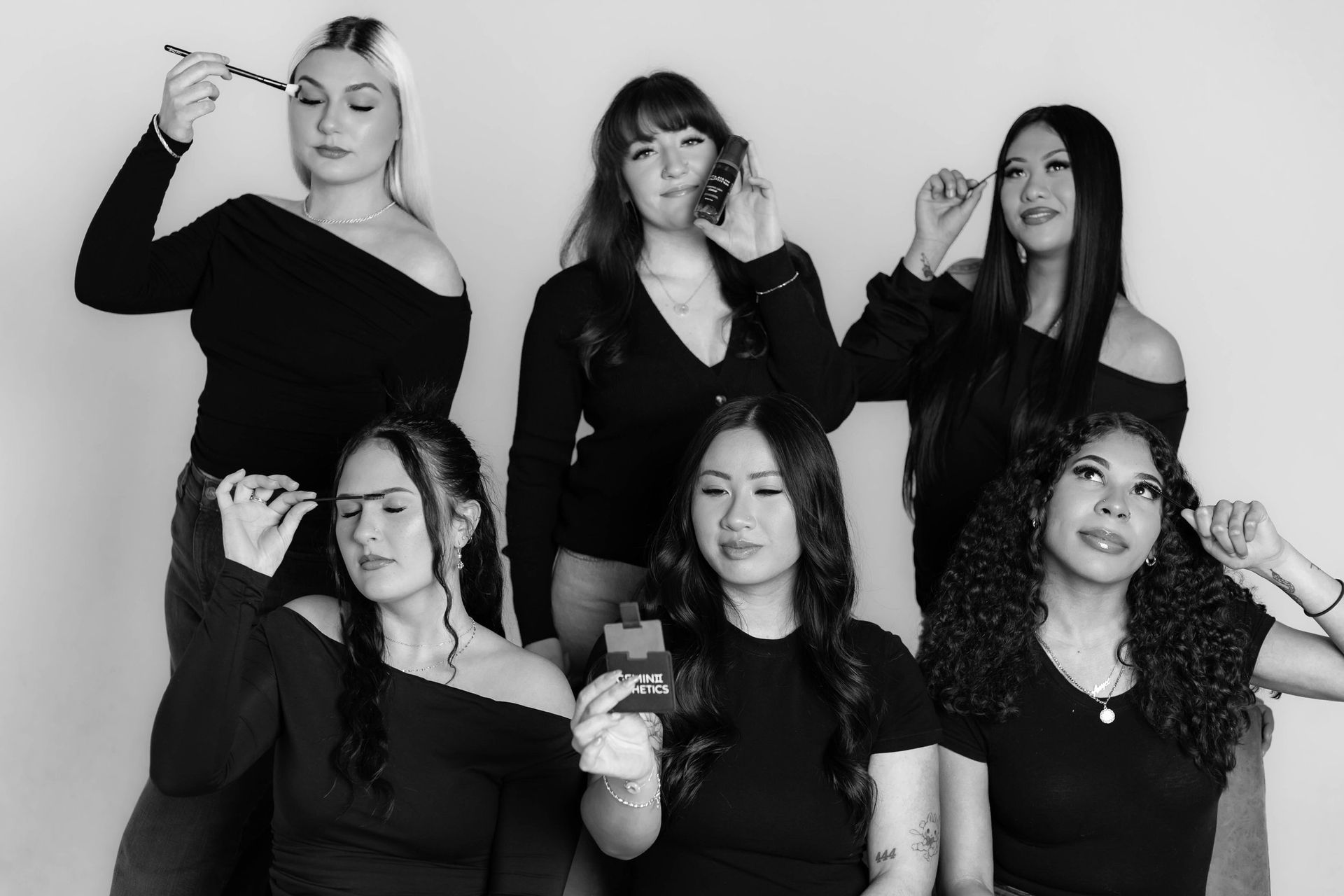 Six women in black tops holding tools, posing together in a studio.
