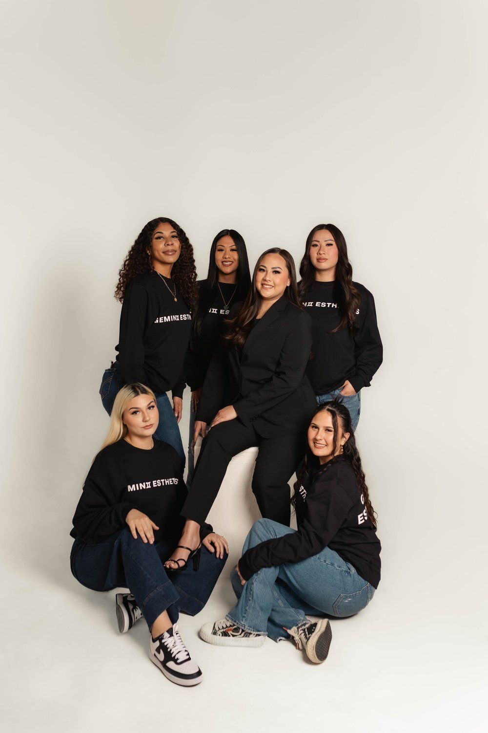 Group of people wearing black sweatshirts and jeans, posing on white background.