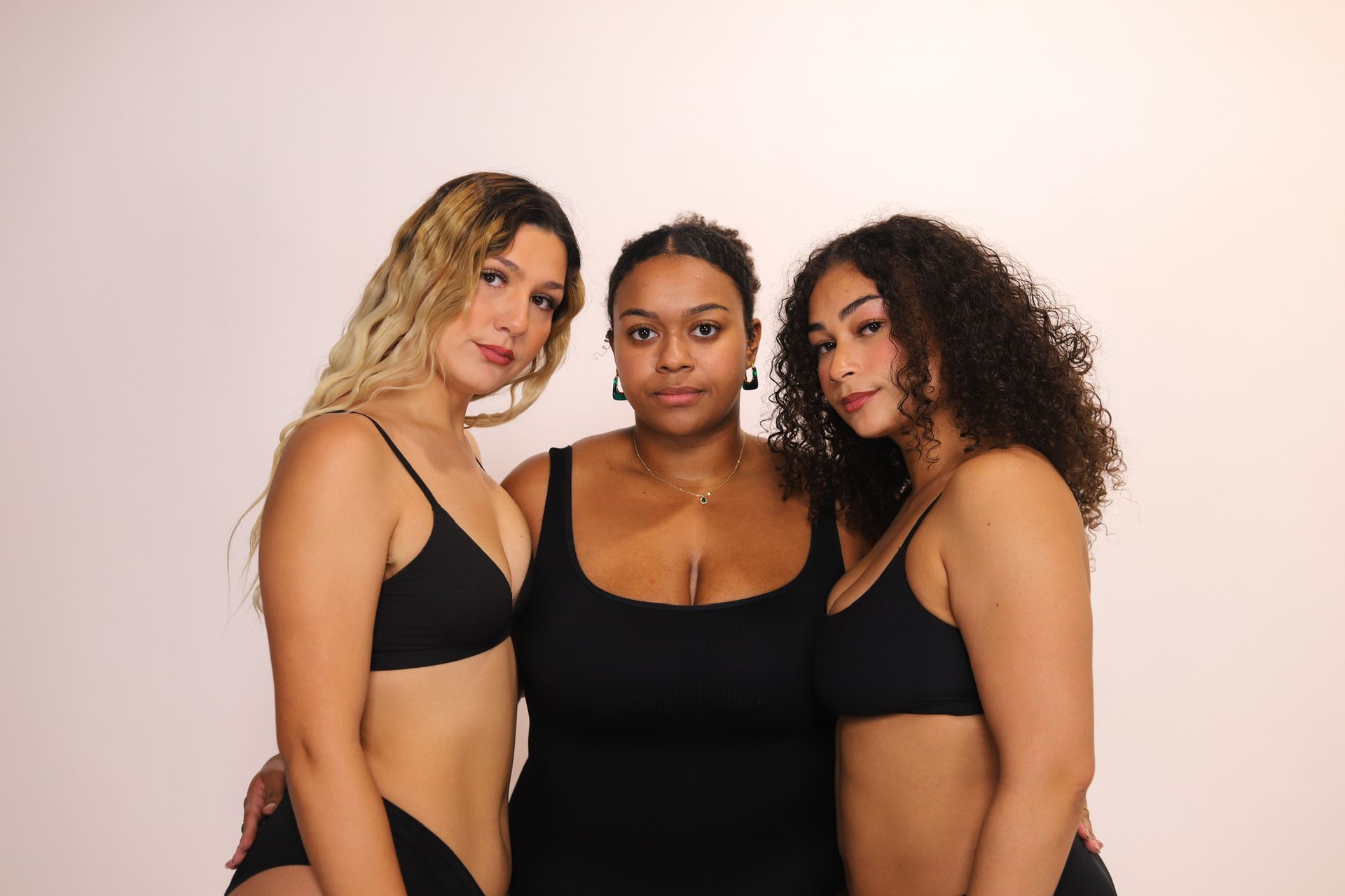 Three people in black swimwear pose against a light pink backdrop.